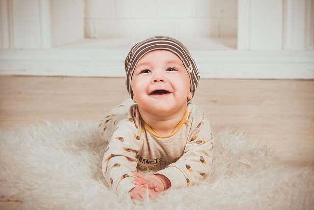 Adorable newborn baby lying on a soft white rug, wearing a striped knit hat and light outfit with brown patterns, against a cozy wooden floor and white wall backdrop—perfect representation of peaceful early childhood moments.